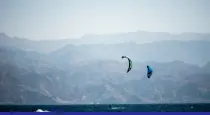 Two kitesurfers on a body of water with distant mountains